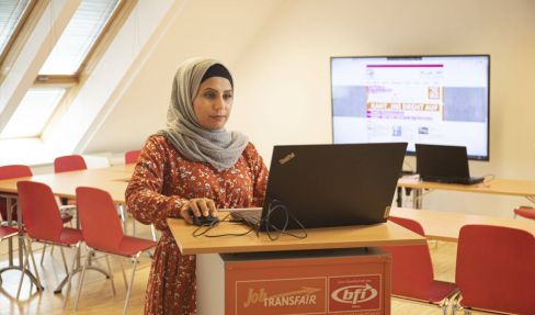 Eine unserer Teilnehmerinnen steht in einem Raum vor einem Laptop und arbeitet mit diesem Laptop.