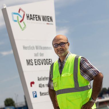 Baber Ashraf posiert vor dem Logo von Hafen Wien.