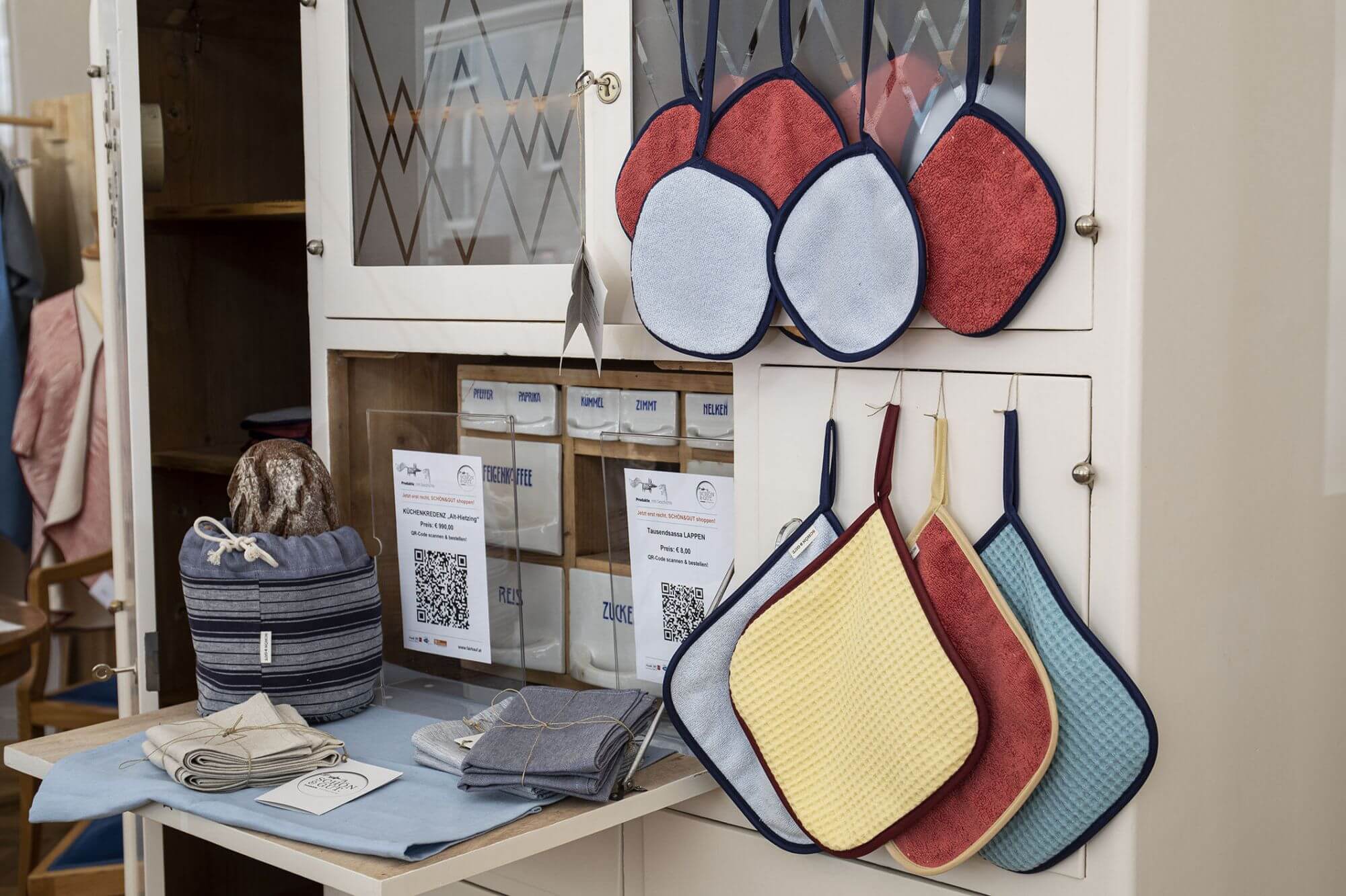 Verschiedene Topflappen, eine Tasche und andere Textilien sind in unserem Social Concept Store Schön und Gut zum Verkauf ausgestellt.